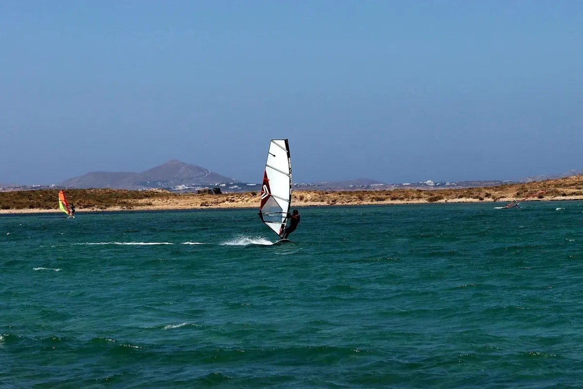 Windsurfer płynący na desce po jeziorze, wykorzystujący siłę wiatru do żeglugi.